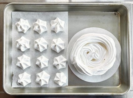 Meringue piped into a dozen kisses, plus one 5" round, on a baking sheet, ready to bake.